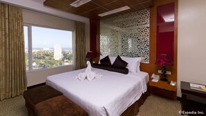 A hotel room with a large bed, a view of the city, a wooden ceiling, and a patterned wall. - Hotel Elizabeth Cebu (Cebu City)