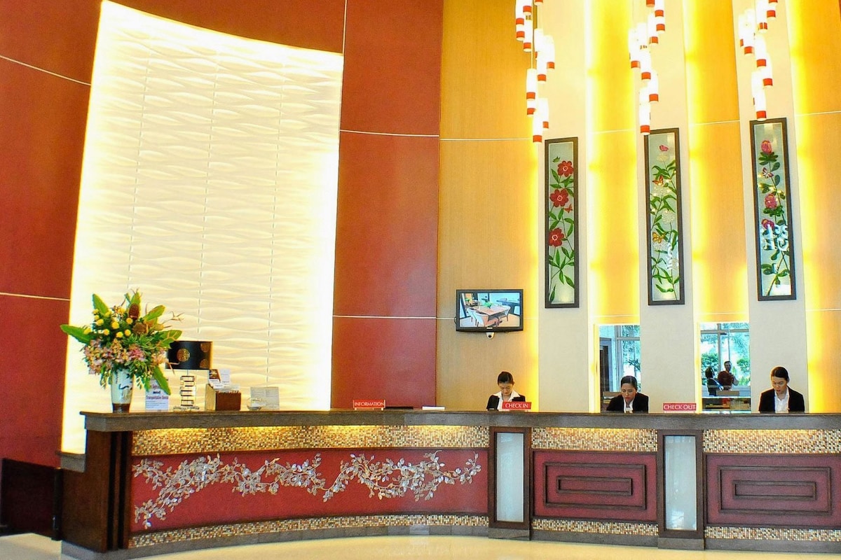 A hotel reception area with a check-in counter, information desk, and decorative floral panels.