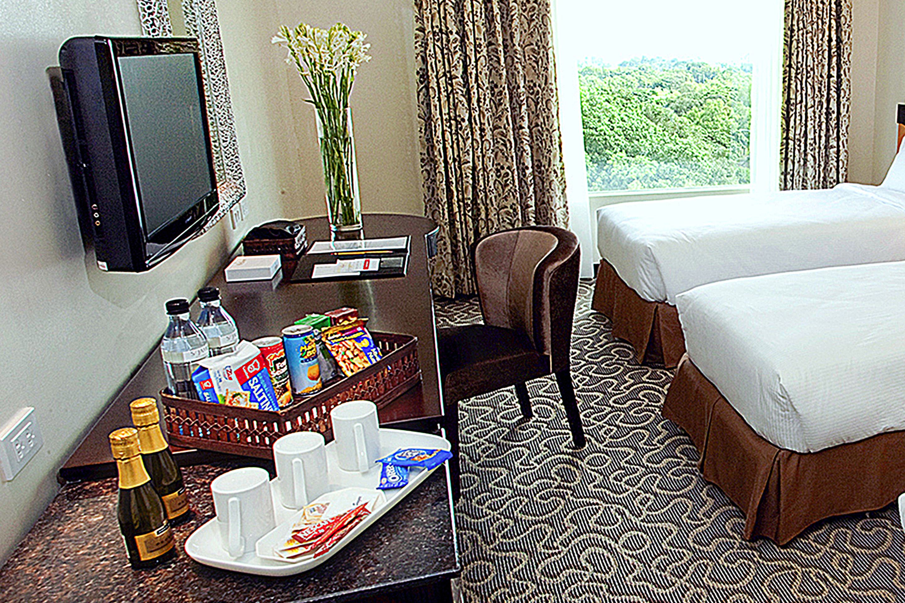 Habitación de hotel con cama, televisor, escritorio y bandeja de desayuno, y vista a zonas verdes.