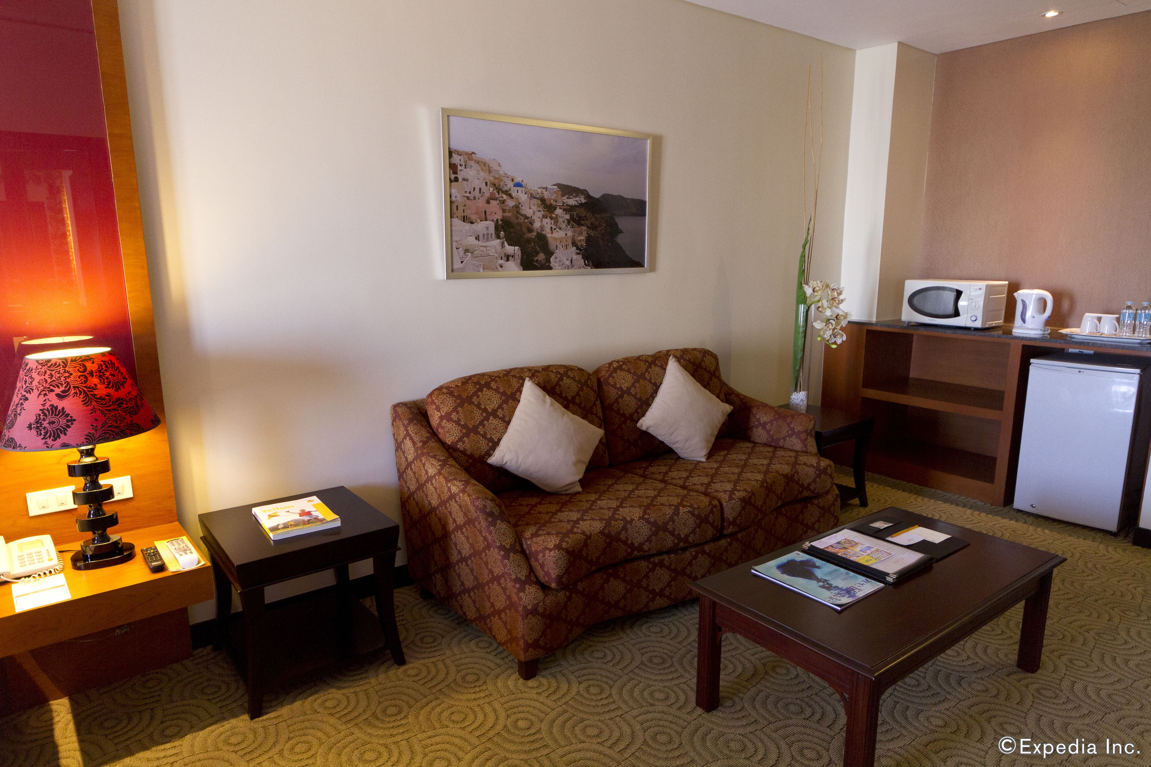 A hotel room with a patterned sofa, a small table with a lamp, a coffee maker, and a microwave on a counter.