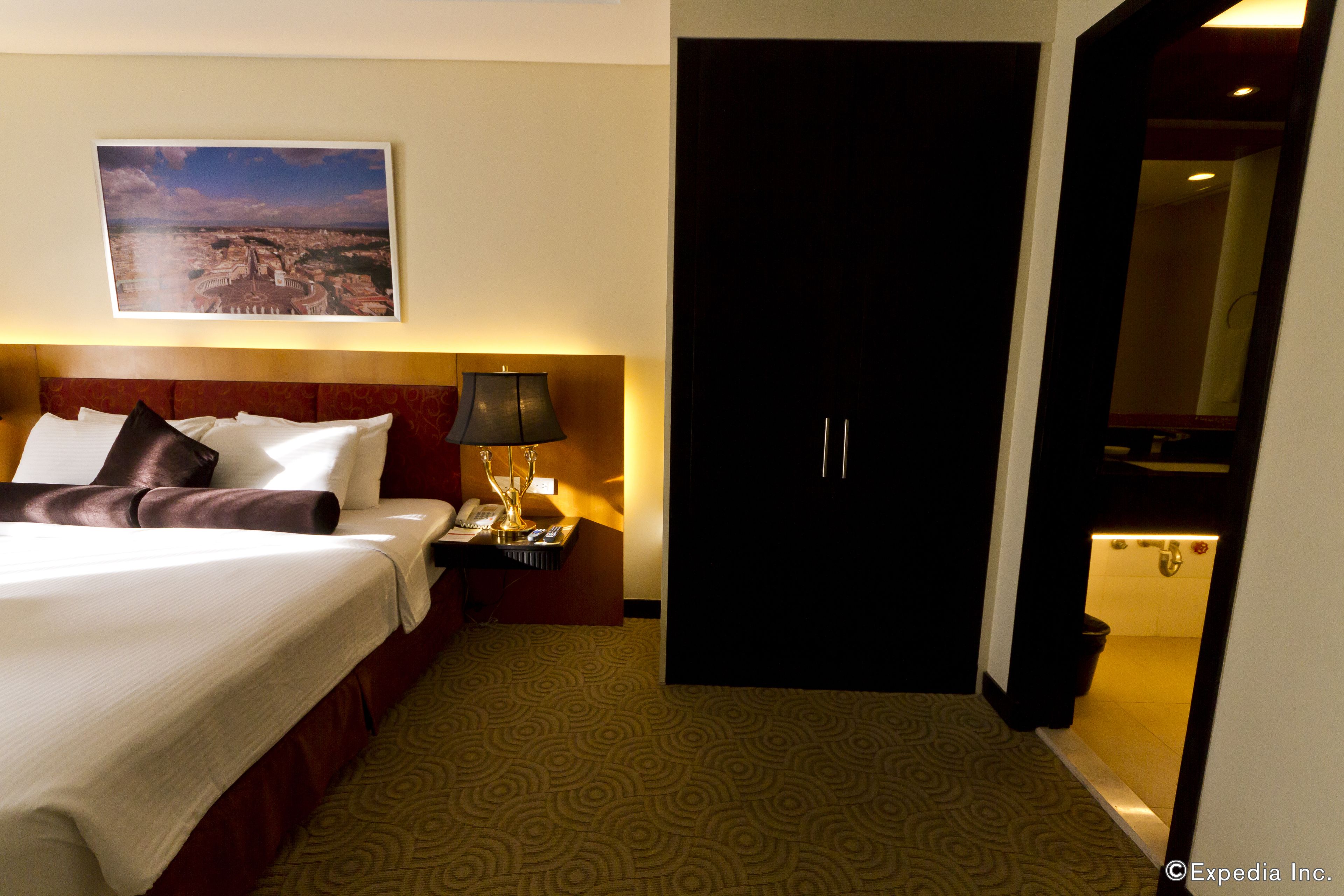 Une chambre d’hôtel avec un lit, une table de chevet, une lampe, une porte et une salle de bain visible à travers une porte ouverte.
