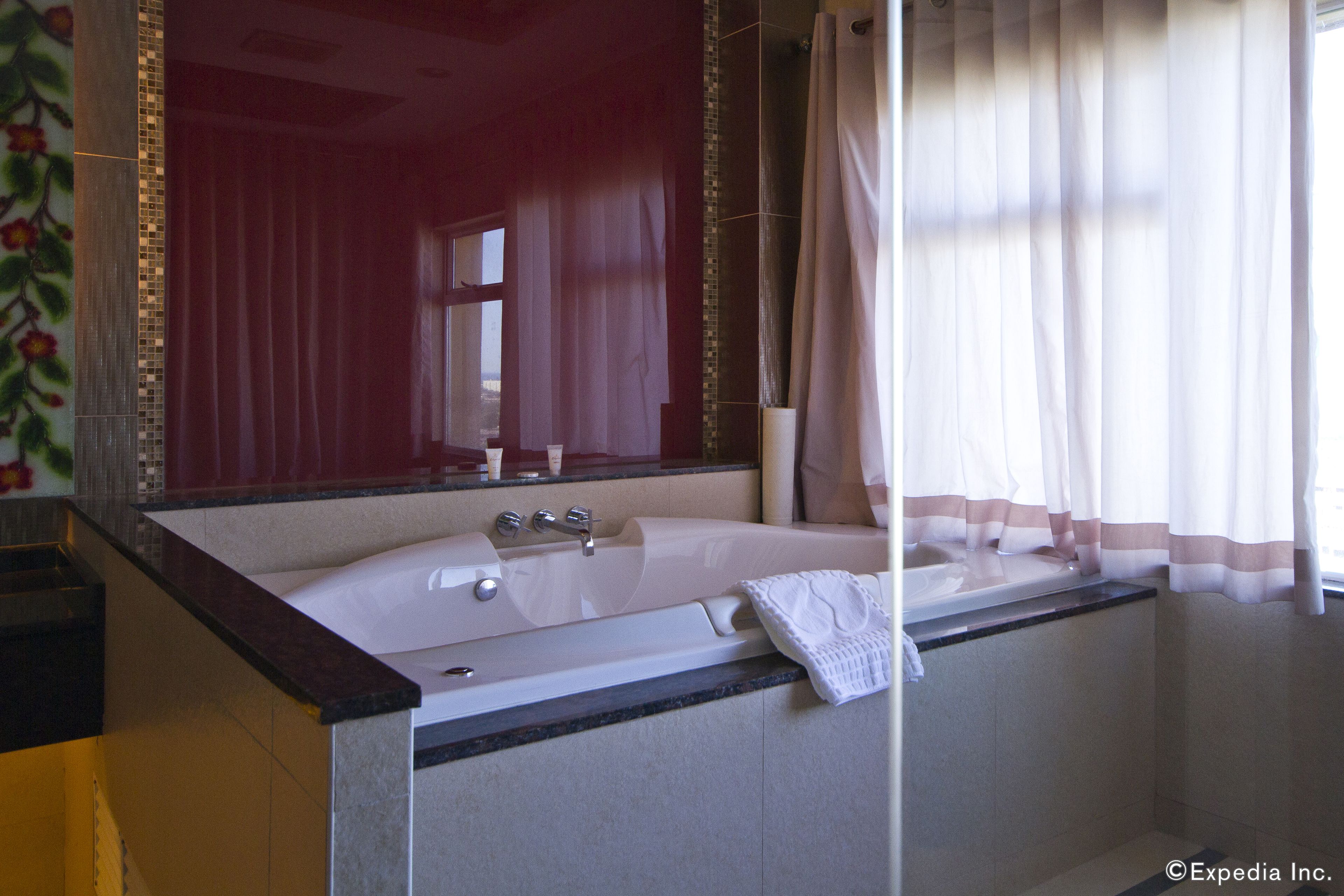 Une salle de bain avec une grande baignoire, un miroir et une fenêtre avec des rideaux.