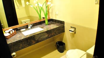 A bathroom with a granite countertop, a white toilet, a black trash can, and a mirror with a decorative frame.