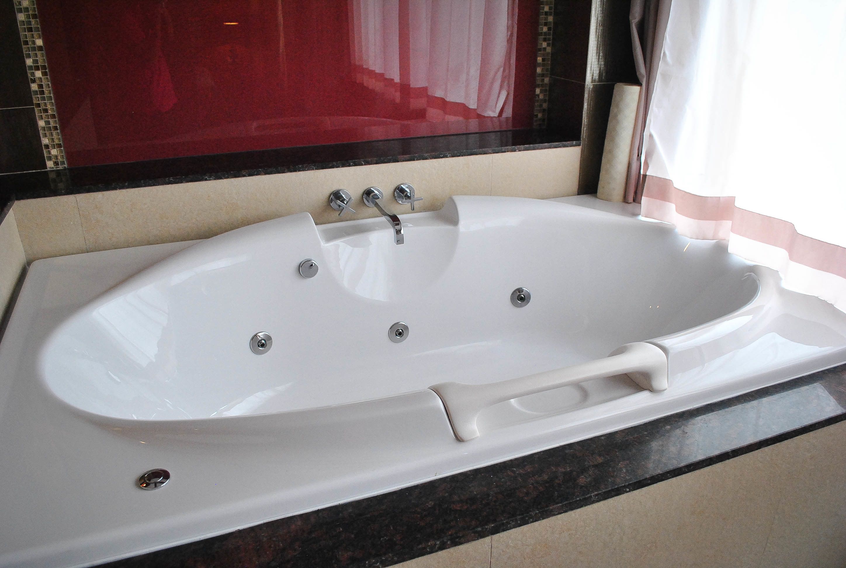 Eine weiße Badewanne mit Chromarmaturen in einem Badezimmer mit dunkler Ablage und einer Wand aus roten Fliesen.