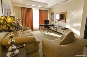 Habitación de hotel con dos sofás, un escritorio, un televisor y una lámpara.
