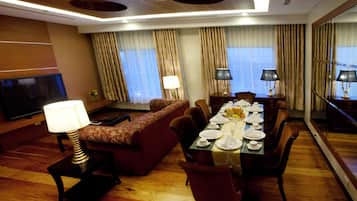 Una camera d'albergo con zona pranzo, divano, televisore e un grande specchio.