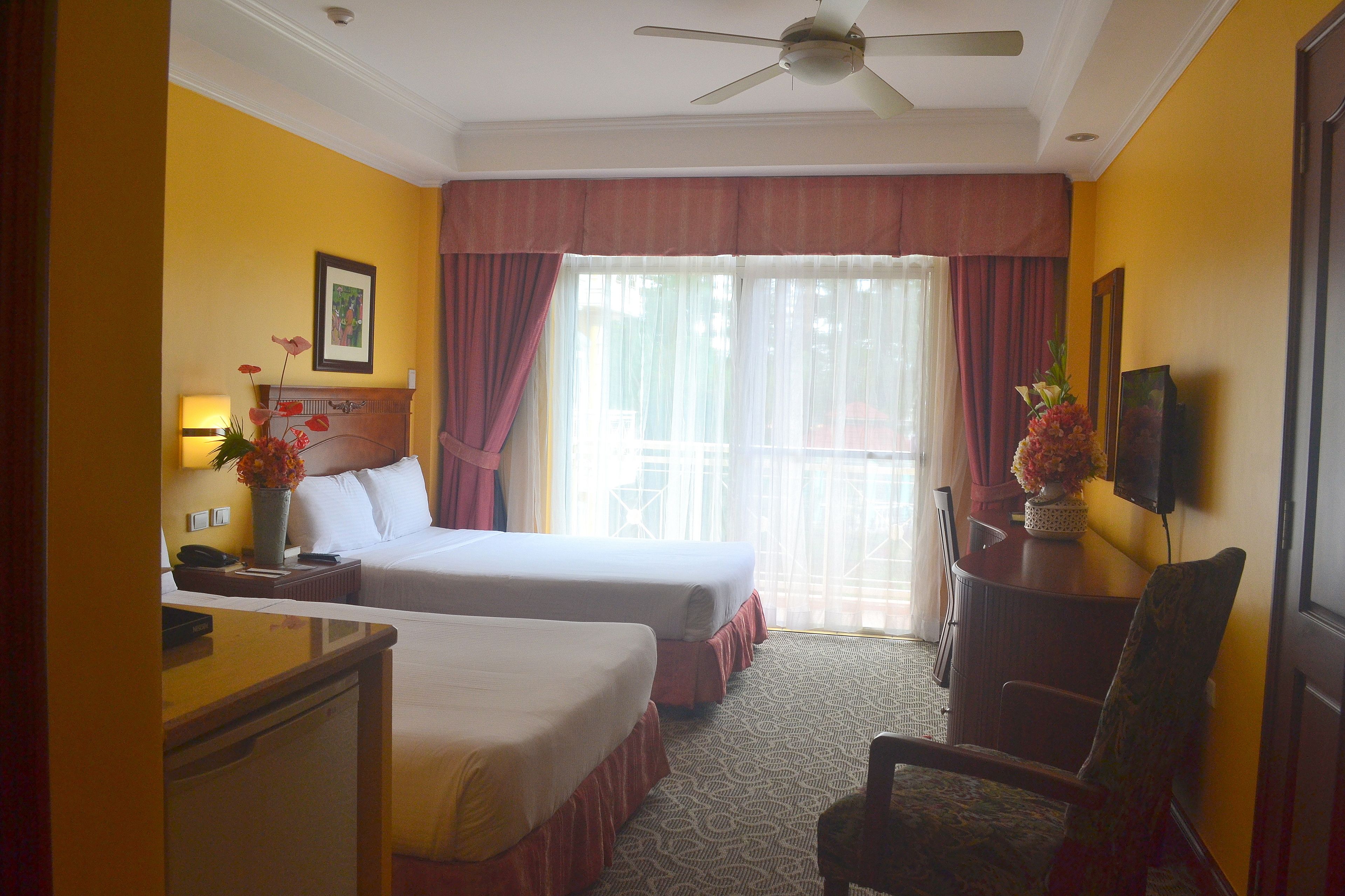 A hotel room with two beds, a desk, a chair, a television, and a window with curtains.
