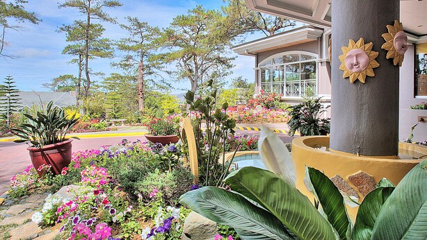 A landscaped area with potted plants and flowers, a building with a large column, and a clear sky. - Hotel Elizabeth Baguio (Baguio)