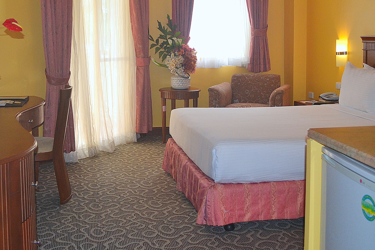 A hotel room with a bed, a desk, a chair, a small table, a lamp, and a ceiling fan.