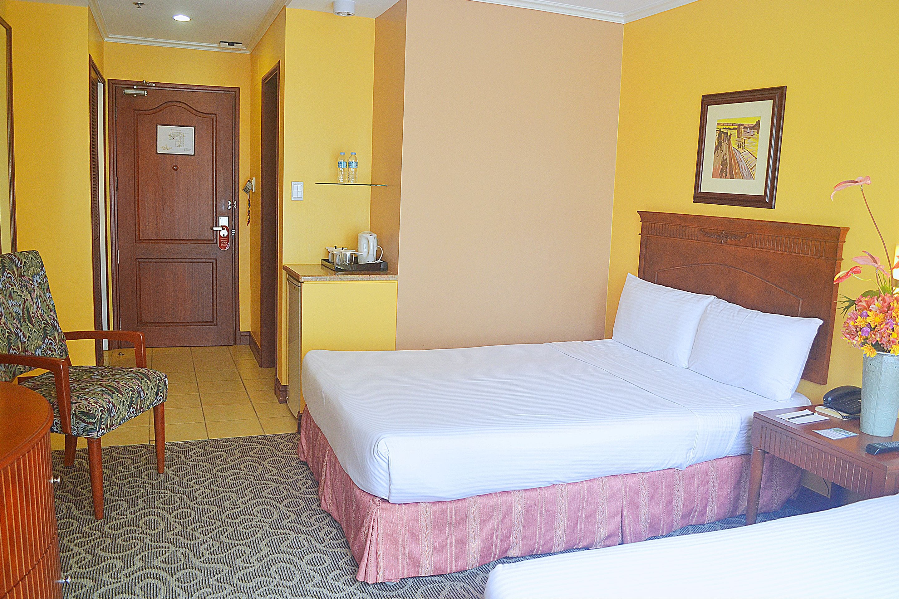 A hotel room with a bed, a chair, a desk with a telephone, and a picture on the wall.
