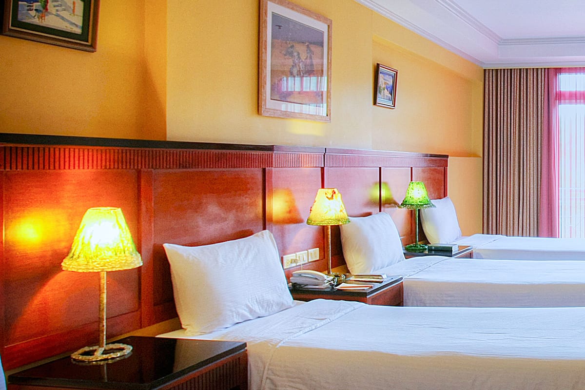 A hotel room with two beds, a wooden headboard, bedside lamps, and a framed picture on the wall.