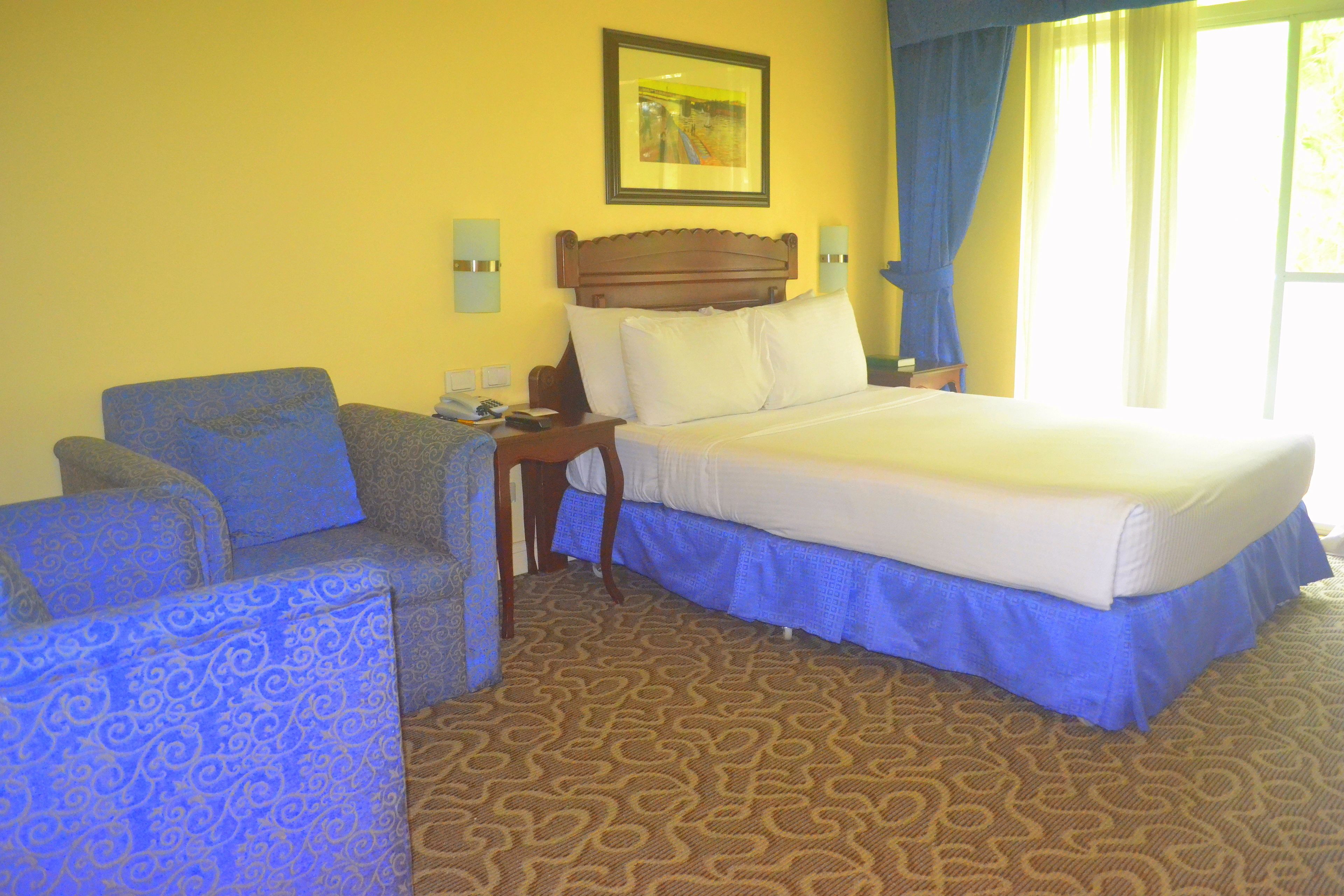 A hotel room with a bed, a chair, a nightstand, and a wall-mounted picture.
