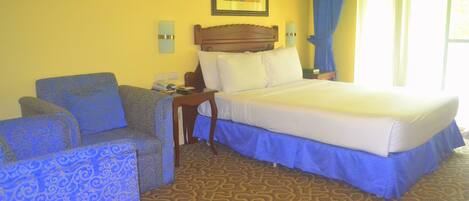 A hotel room with a bed, a chair, a nightstand, and a wall-mounted picture.