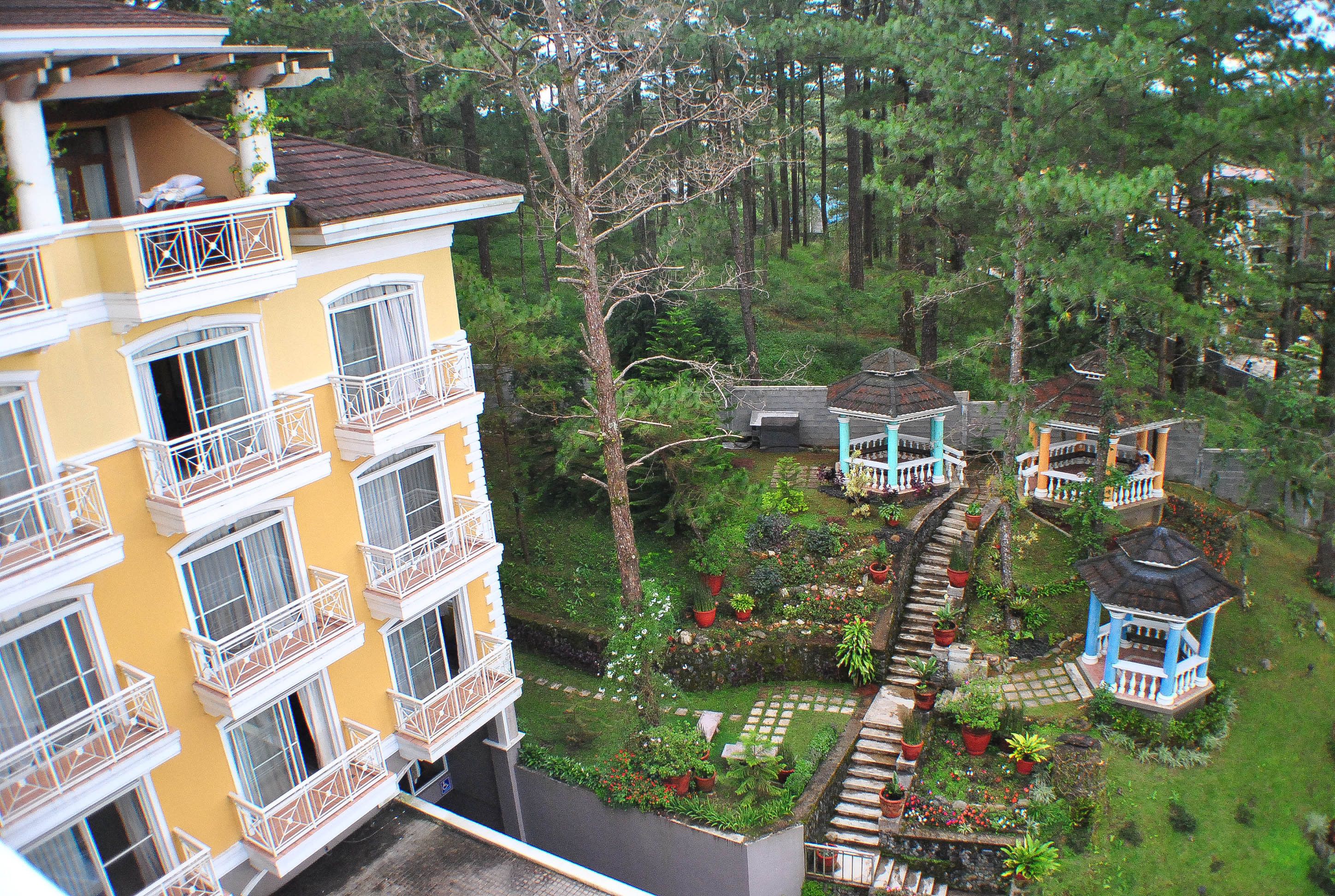 Un edificio de varios pisos con balcones, un jardín con plantas en macetas y un mirador.