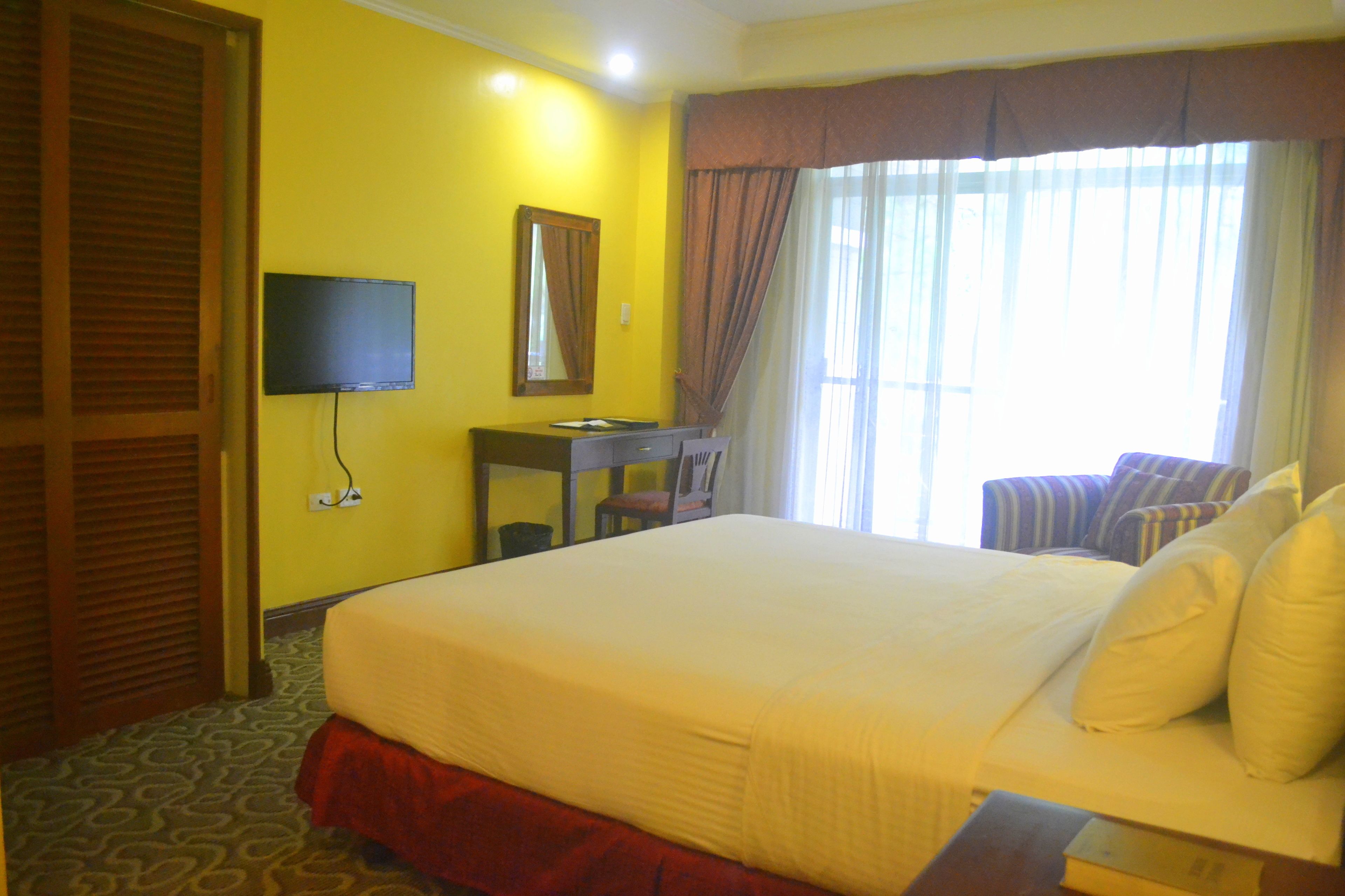 Una habitación de hotel con una cama grande, un escritorio, una silla, un televisor y una ventana con cortinas.