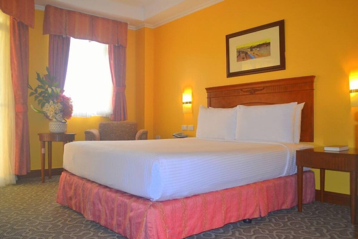 A hotel room with a large bed, a desk, a chair, a lamp, and a picture on the wall.
