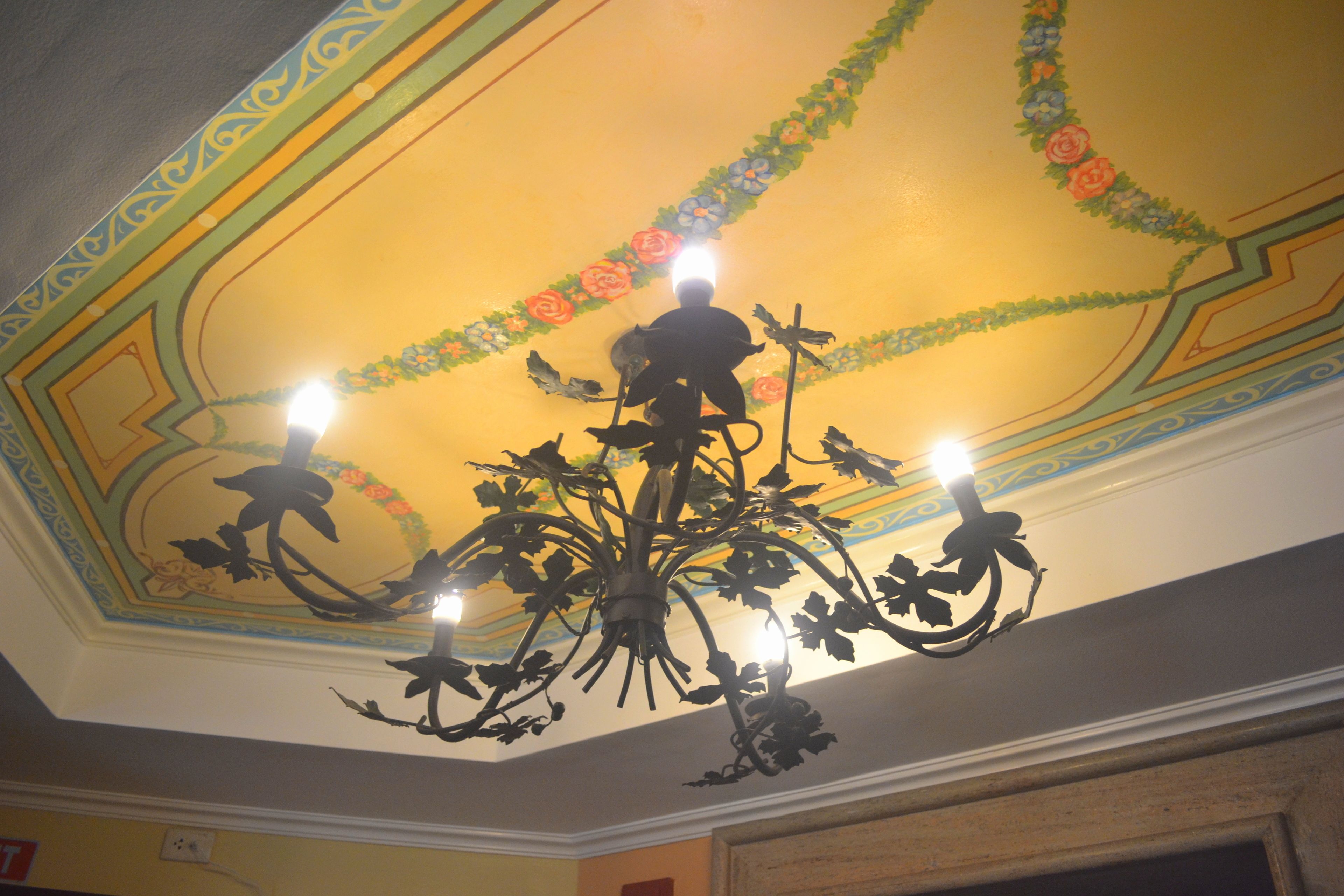 Un candelabro con múltiples fuentes de luz y un techo decorativo con motivos florales.