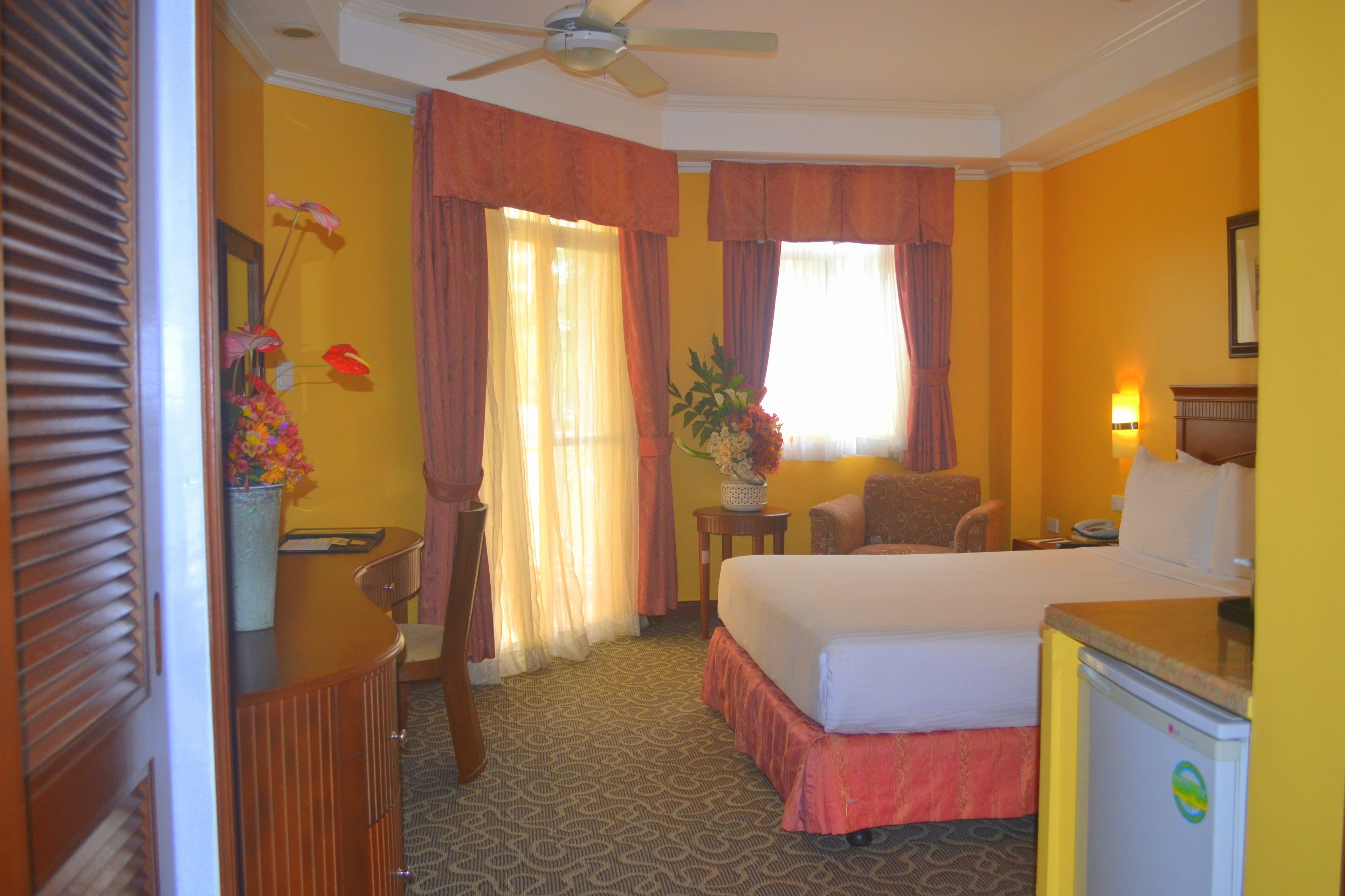 A hotel room with a bed, desk, chair, and a small refrigerator.