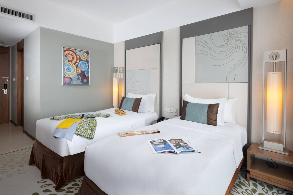 Habitación de hotel con dos camas, un cuadro abstracto grande, una lámpara moderna y una revista sobre la cama.