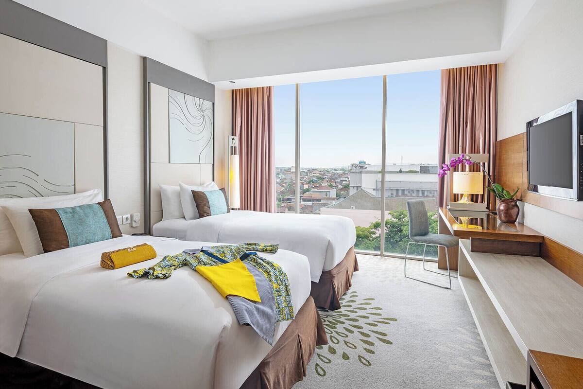 Habitación de hotel con dos camas, un escritorio, televisión y vista a la ciudad.