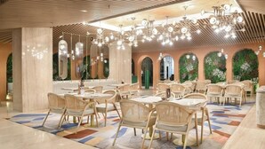 Un comedor espacioso con múltiples mesas y sillas, piso estampado y techo con lámparas colgantes.