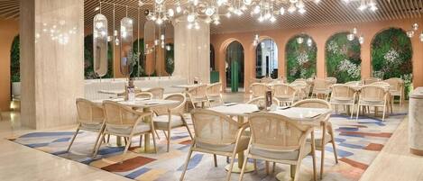 A spacious dining area with multiple tables and chairs, a patterned floor, and a ceiling with hanging lights.