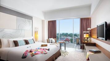 Habitación de hotel con una cama grande, un escritorio, una silla, un televisor y vistas a la ciudad.