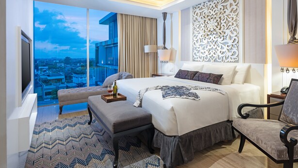 Una habitación de hotel moderna con una cama grande, una zona de estar, vistas de la ciudad y un panel decorativo en la pared.