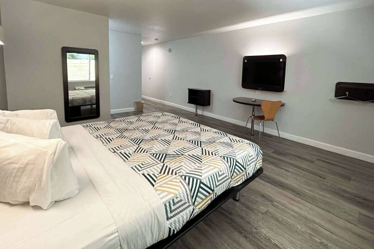 A modern hotel room with a large bed, a small table, a chair, a TV, and a mirror.
