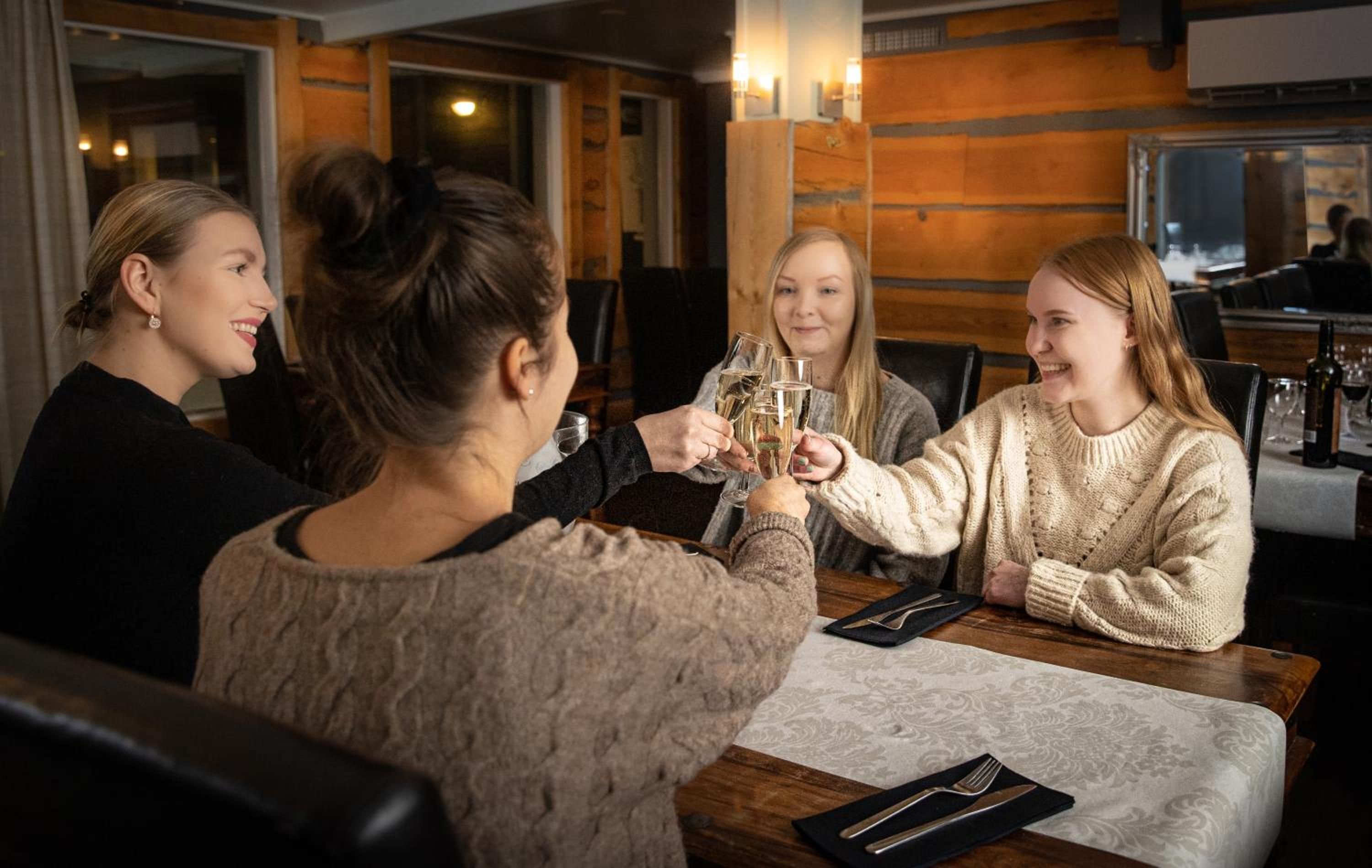 A group of people toasting with glasses at a wooden table in a restaurant with a view of the city.