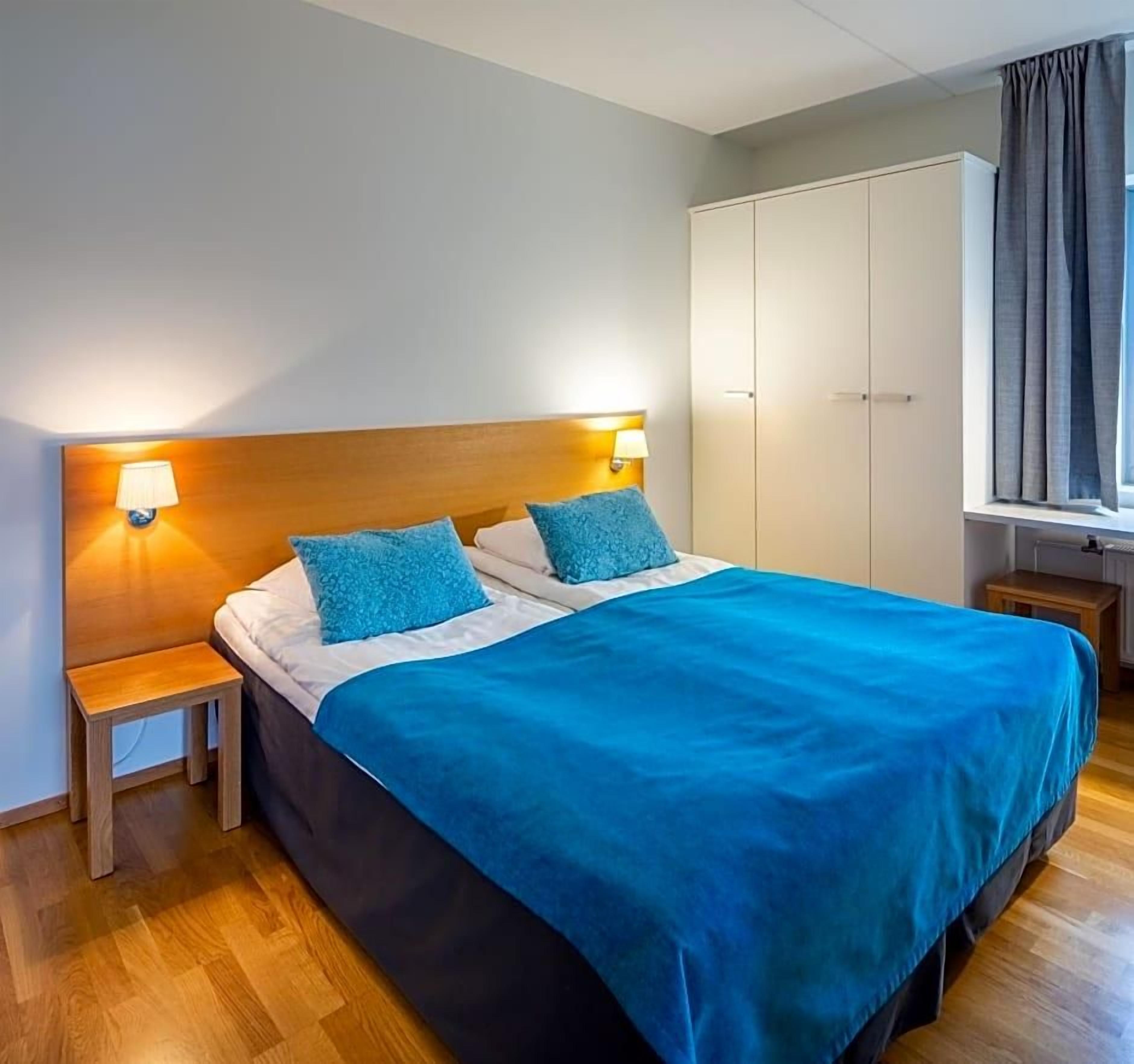 Ein Hotelzimmer mit Bett, Nachttischlampen, einem Kleiderschrank und einem Fenster mit Vorhängen.
