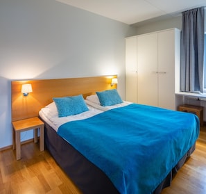 A hotel room with a bed, two bedside lamps, a wardrobe, and a window with curtains.