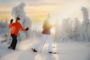 Dos personas esquiando en un sendero cubierto de nieve, con árboles al fondo.