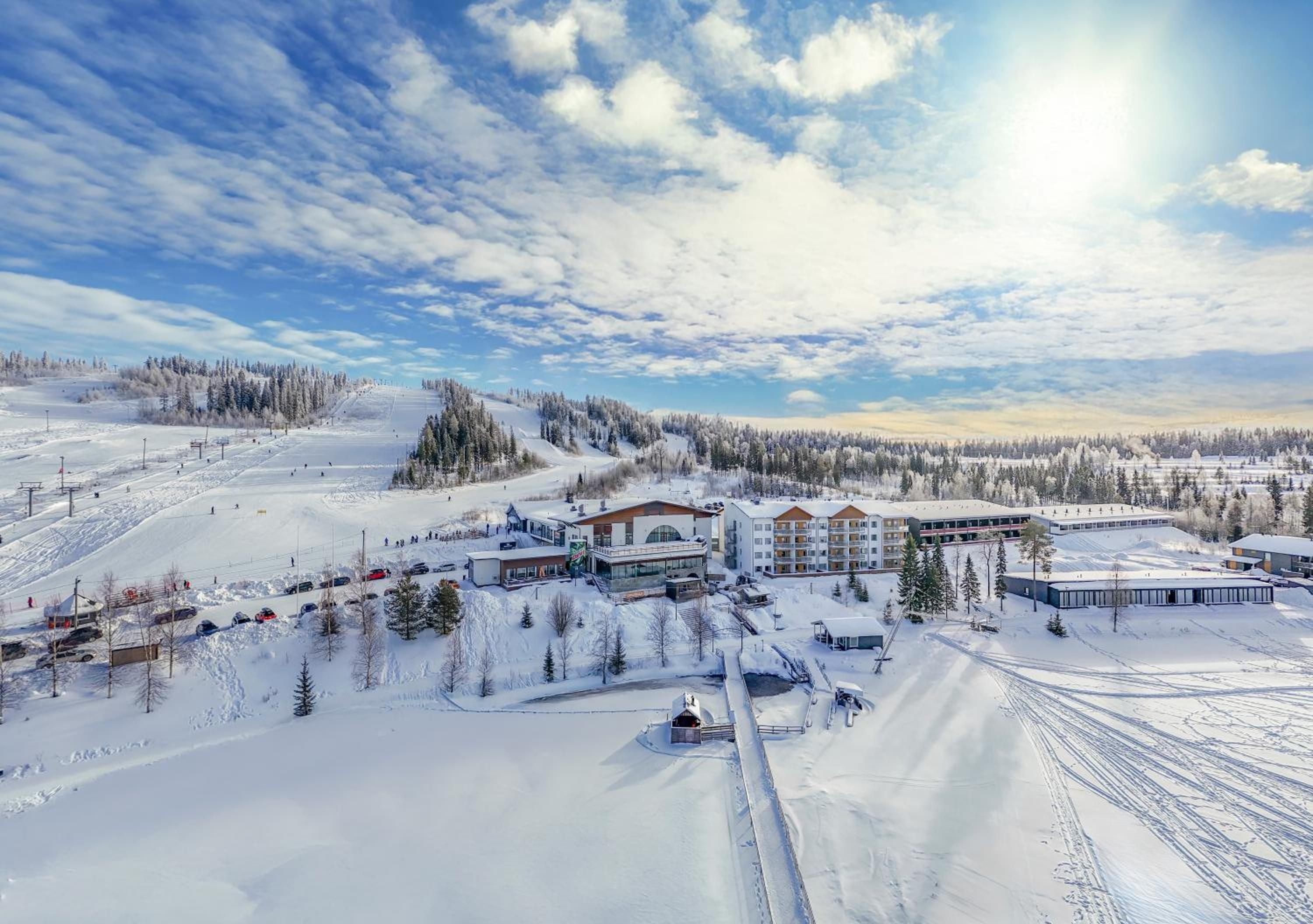 Une station de ski enneigée, dotée de plusieurs bâtiments, dont un hôtel au design moderne, de remontées mécaniques et offrant une vue dégagée sur le paysage enneigé environnant.