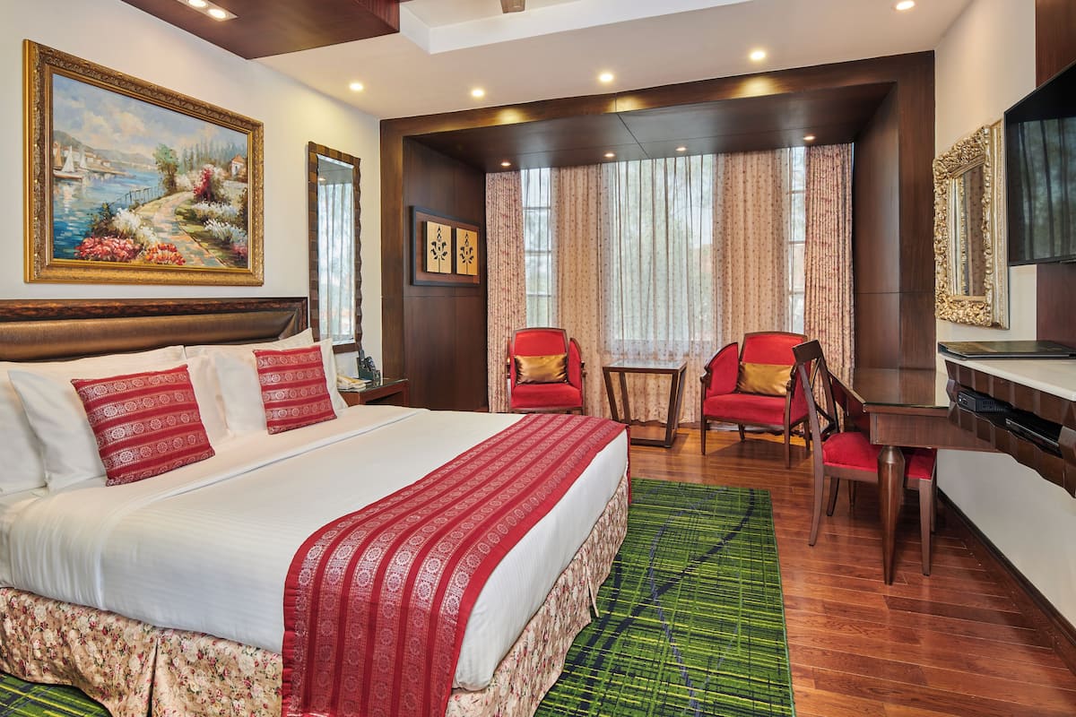 A hotel room with a large bed, a desk, a chair, and a painting on the wall.