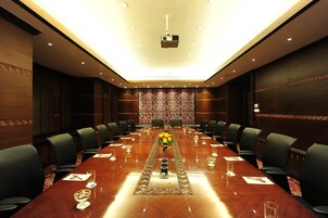 Un salón de conferencias con una larga mesa, sillas y un proyector.