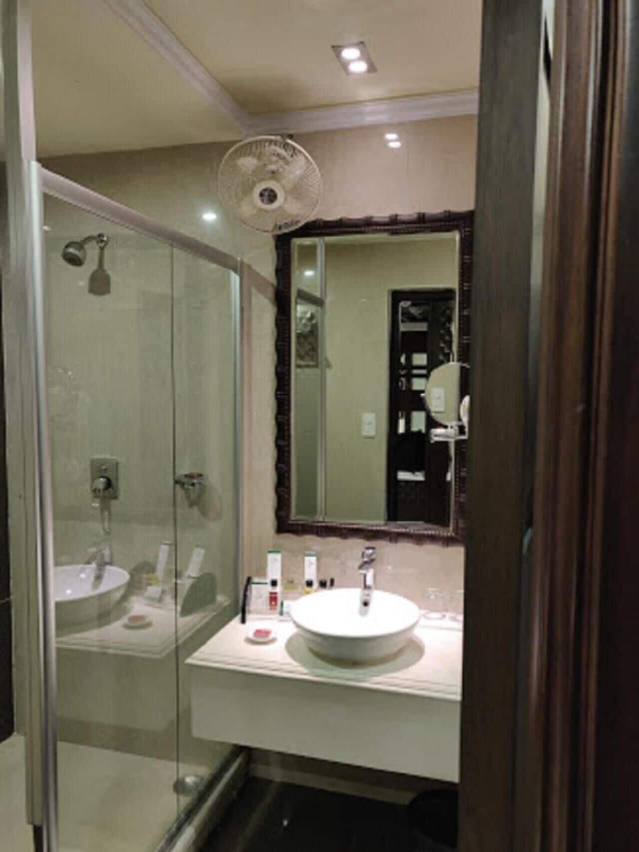 Un baño con ducha envuelta en vidrio, un lavamanos blanco y un espejo con marco decorativo.