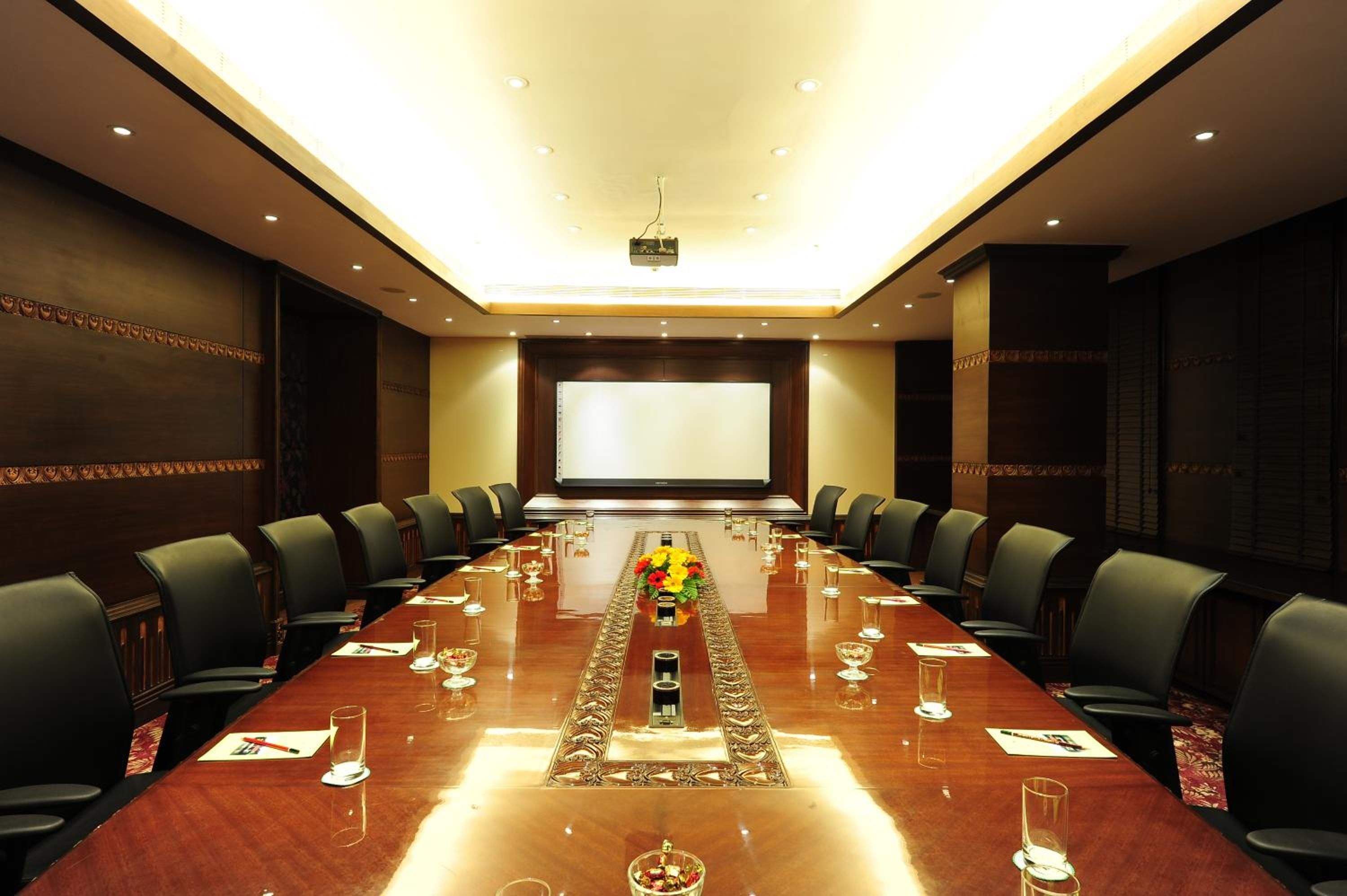 A conference room with a long table, chairs, a projector screen, and a floral centerpiece.