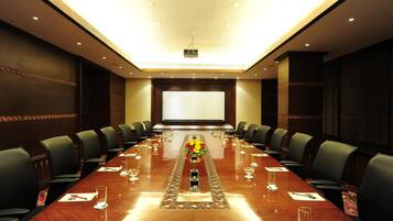 A conference room with a long table, chairs, a projector screen, and a floral centerpiece.