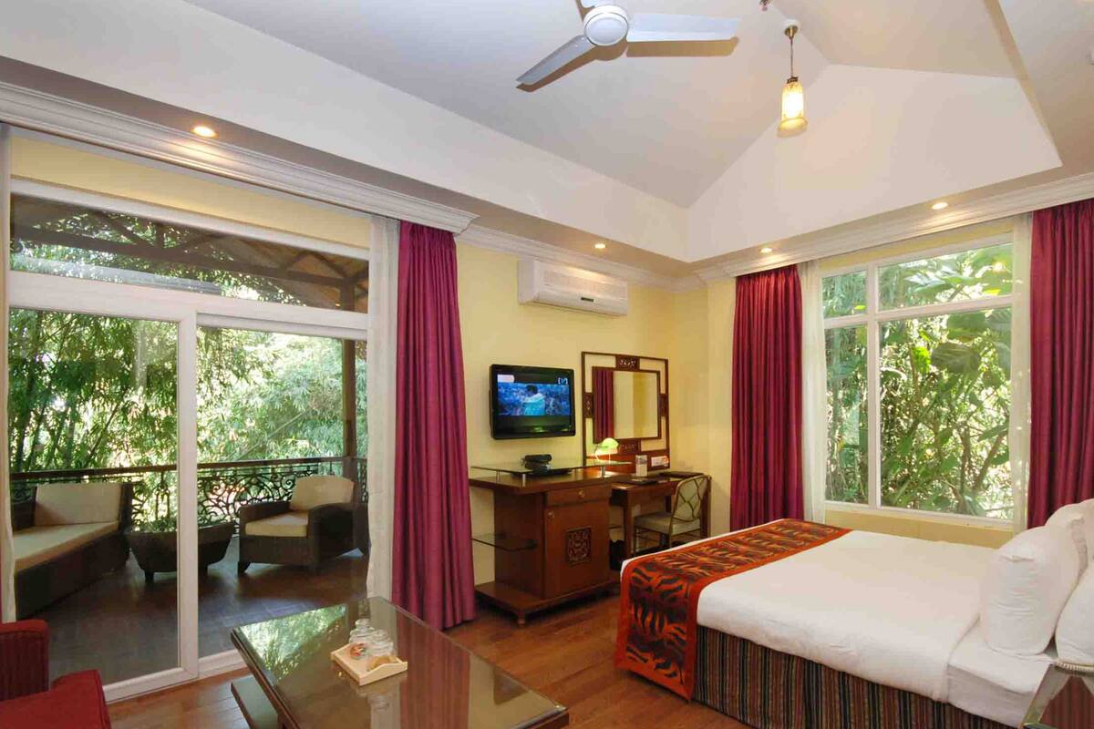 A hotel room with a bed, a desk, a television, and a balcony with seating.