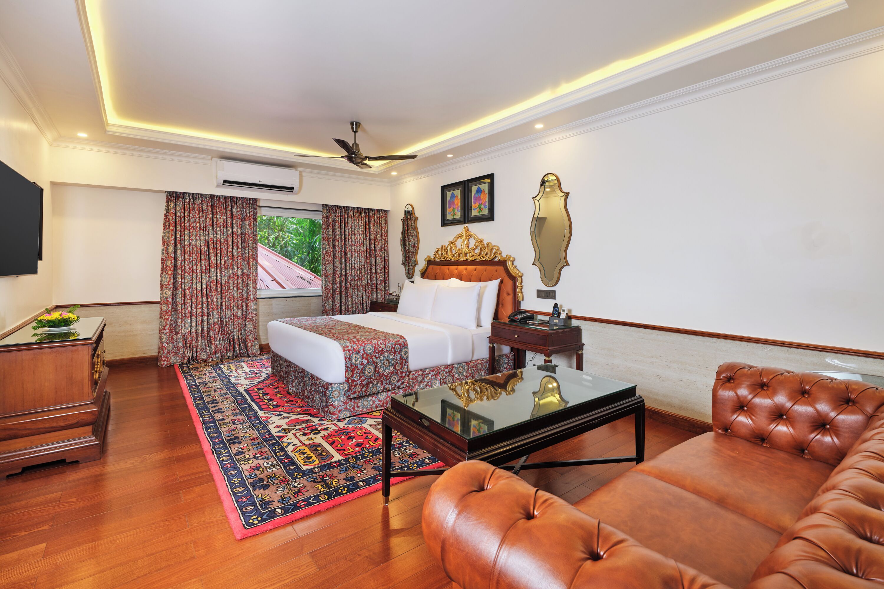 A hotel room with a bed, a sofa, a coffee table, a TV, and a ceiling fan.