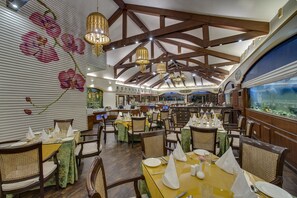 A restaurant with wooden beams, chandeliers, and a large aquarium. Tables are set with white napkins and silverware. - Mayfair Spa Resort & Casino Gangtok (Gangtok)