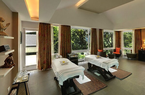 A spa room with two massage tables, a sofa, and a small table with a statue.