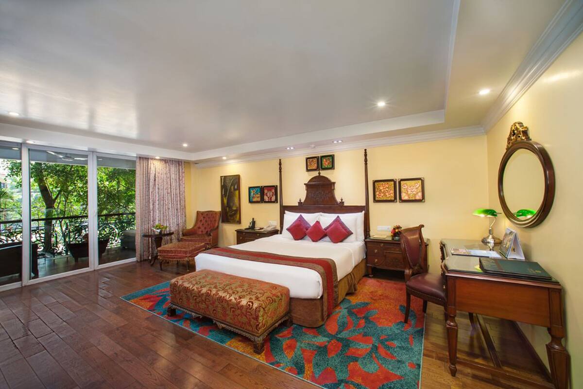 A spacious bedroom with a large bed, a desk, a chair, and a balcony with a view of trees.