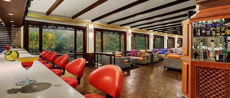 A bar area with red chairs, a bar counter, and a view of greenery through large windows.