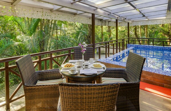 A balcony with wicker furniture, a dining table set with plates, cups, and a vase of flowers.