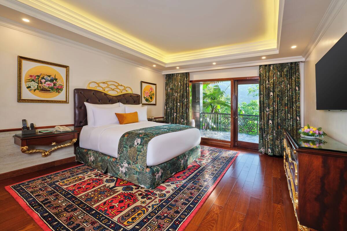 A spacious bedroom with a large bed, a wooden floor, and a balcony with curtains.