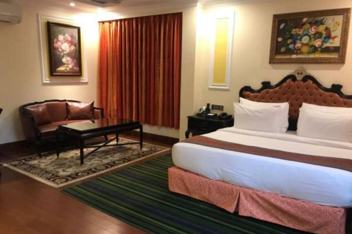 A hotel room with a large bed, a desk, a chair, a nightstand, and a painting on the wall.