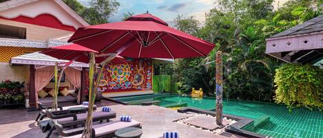 A poolside area with lounge chairs, a red umbrella, and a decorative wall.