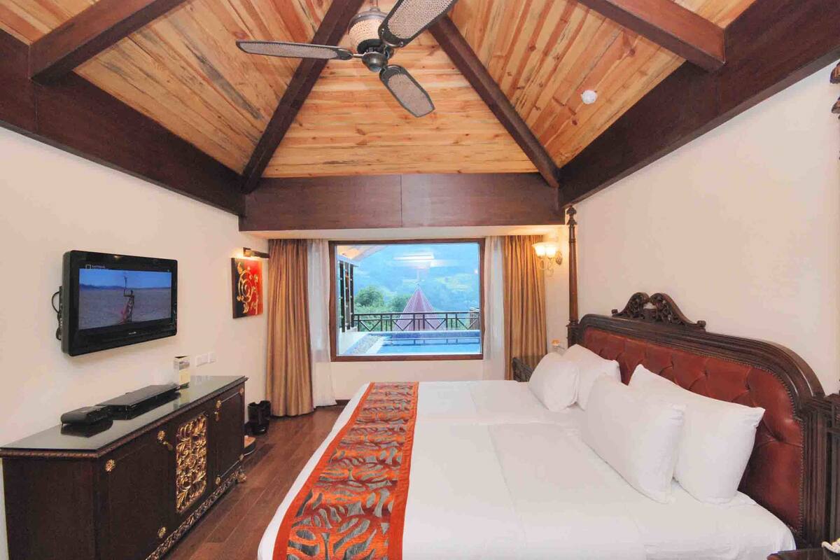 A bedroom with a large bed, a television on a cabinet, and a balcony with a view.